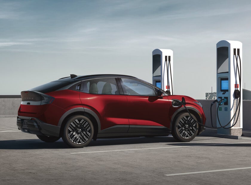 2026 Nissan LEAF PLATINUM+ in Coulis Red Pearl/Super Black charging at a public EV station under a clear sky.