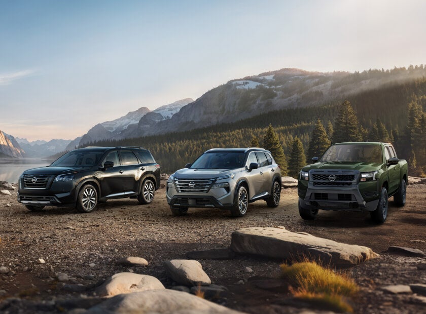 2026 Nissan Rogue, Pathfinder and Frontier posed on rocky terrain beside a mountain lake at sunrise.