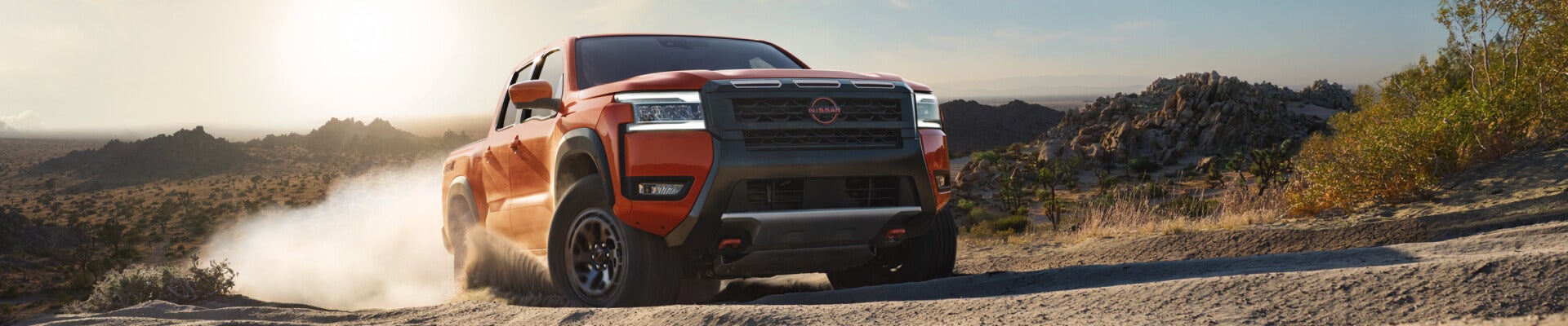 Front three-quarter view of an orange Nissan Frontier PRO-4X on a dusty desert trail.E